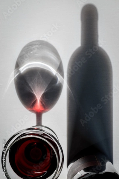 Fototapeta Glass of red wine and bottle with shadows and reflections on a white textured surface. High angle view.