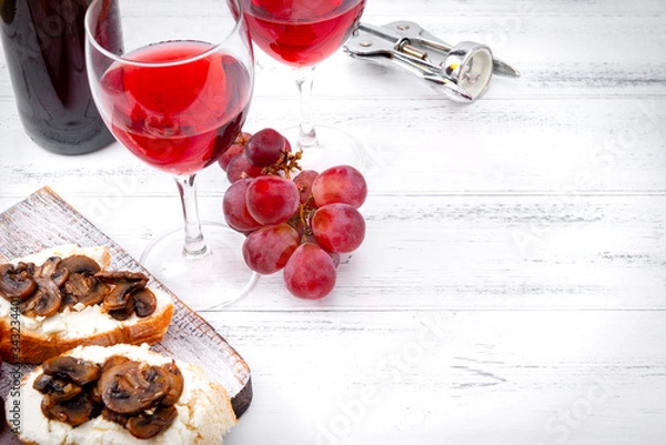 Fototapeta glasses of red wine, ,  bottle  , grapes, corkscrew,  snacks with mushrooms  and  cheese   on a white wooden background, copy space,