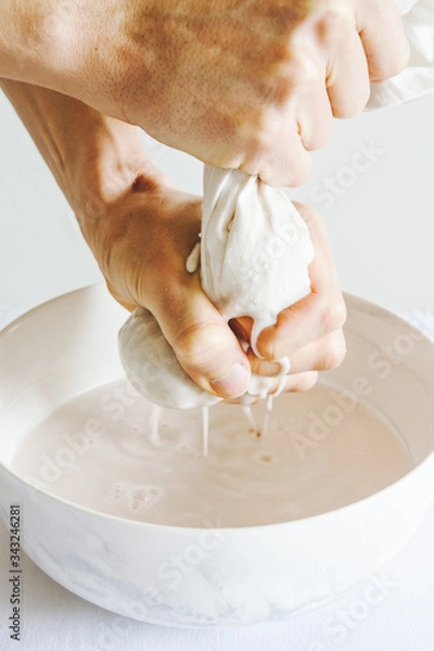 Fototapeta Preparation of a plant-based nut milk with hands straining the milk through a milk bag. White background