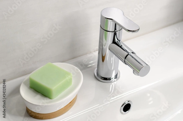 Obraz Soap in a soap dish on a white sink in the bathroom next to a chrome faucet.