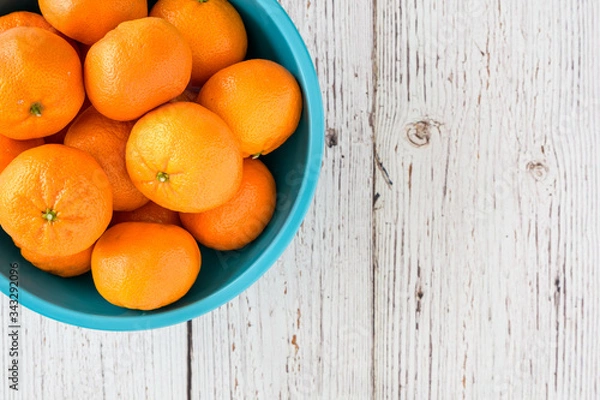 Fototapeta Small clementine oranges in a light blue bowl on a whitewashed wood background
