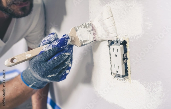 Obraz Painter man with gloves painting the wall around power outlet.