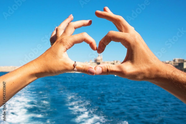 Fototapeta A young couple making heart with hands in rings,symbol of love  from the boat  at beautiful view on Valletta ,Malta