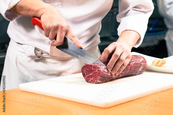 Obraz Chef cutting a large raw boneless beef steak meat on a white cutting board.