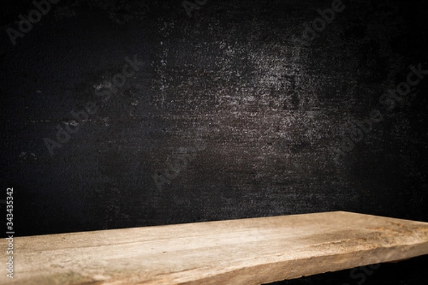 Fototapeta Old wooden table top with a dirty concrete block wall in a dark room background.