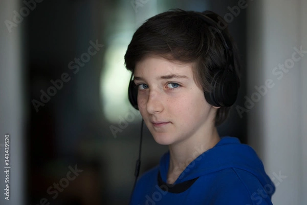 Fototapeta portrait of a tennager with headphones in his room standing and looking straight