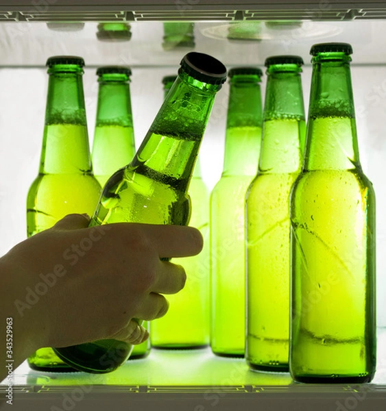 Fototapeta Green beer bottles chilled in drops of water on a shelf in the refrigerator. Hand takes the bottle.