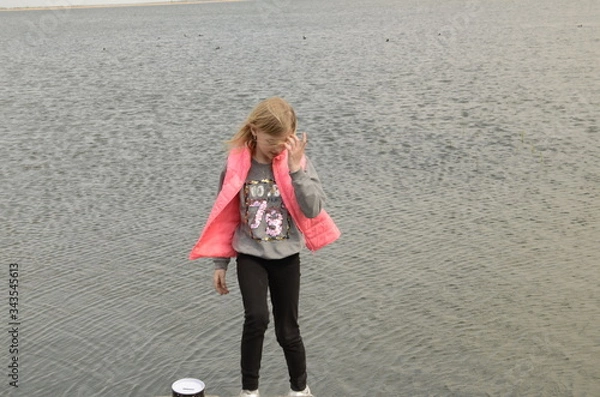 Fototapeta 
Spring. River bank. A girl in a pink vest straightens her hair.