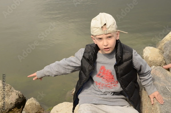 Fototapeta 
Spring. River bank. The boy leaned on a large stone of gray granite.