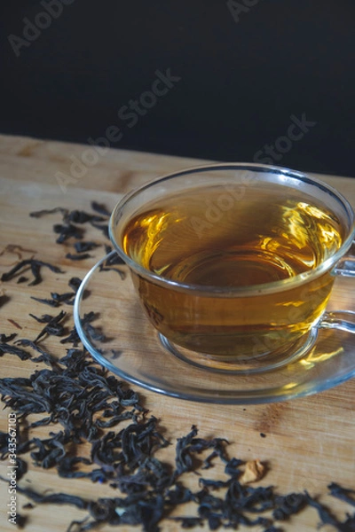 Fototapeta Close up picture cup of tea with dry leaves on the side on wooden background, flat lay composition with empty space for text. Aroma beverage for evening, tea time of chillness, natural taste.
