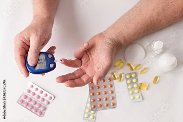 Obraz Old hands with sugar meter. Pills and medicines on the table. Old age. Health care for the elderly.