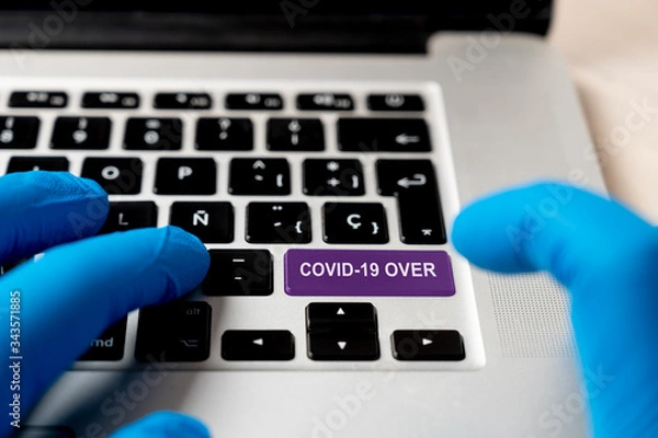 Fototapeta Covid-19 over words on keyboard button. End of coronavirus concept. A finger in a blue medical protective  glove pressing a colored button on notebook