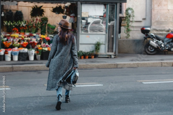 Fototapeta Young beautiful girl tourist crosses the road against the background of a store with bright bouquets and flowers.