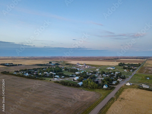 Obraz Drone footage aerial of village in the middle of fields nowhere in Canada Saskatchewan between roads and fields during sunset with blue sky and clouds 