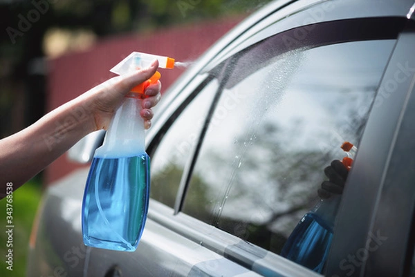 Fototapeta Cleaner is cleaning a car window glass with a rag and detergent close up.