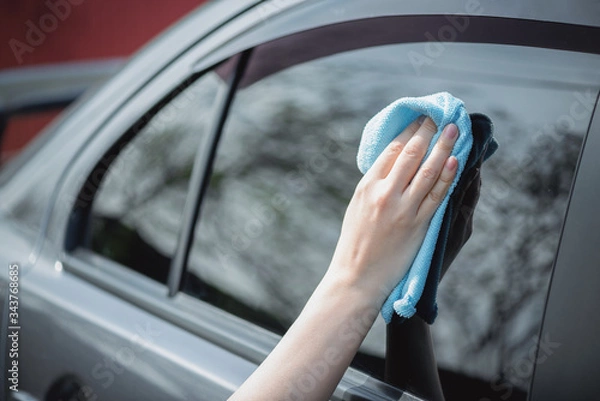 Fototapeta Cleaner is cleaning a car window glass with a rag and detergent close up.