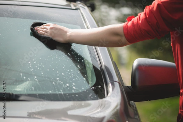 Fototapeta Cleaner is cleaning a car window glass with a rag and detergent close up.