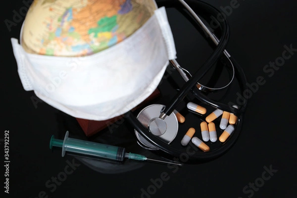 Fototapeta Coronavirus pandemic in world, global quarantine during the COVID-19. Medical mask on globe, stethoscope, syringe and pills on black glass table
