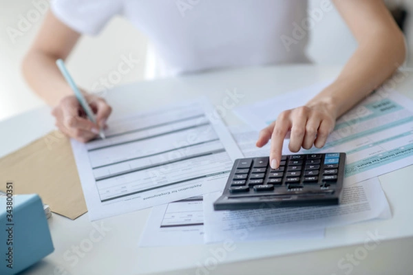 Fototapeta Close-up of female hands pressing buttons on calculator, holding pen