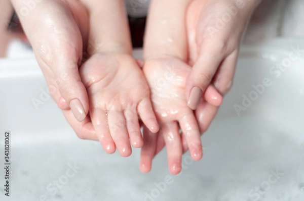 Fototapeta Mom washes hands with soap to her baby. Teaches a child how to wash hands with soap.