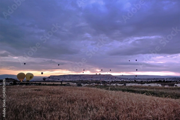 Fototapeta Cappadocia The dawn begins. In the cloudy sky rises many colorful balloons over valleys and gorges. Away the mountains.
