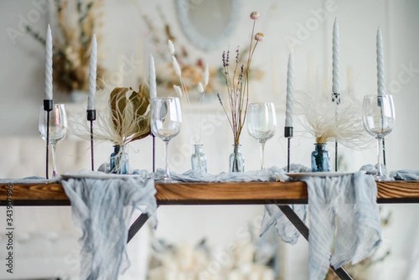Fototapeta Autumn table decoration, wooden table served with dried flower, white plate, vintage cutlery, candeles with bright blue gauze tablecloth. Top view, selective focus.