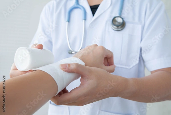 Obraz Doctor bandaging the wrist. Concept of first aids and treatment in wrist injuries. Closeup and selective focus on applying bandage onto patient's hand.