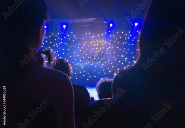 Obraz Blurred view of audience back. Silhouette shot from back in blue light. Multicolored light beams spotlights at the time of the entertainment show. Blurred glowing lights on stage. Small depth of view.