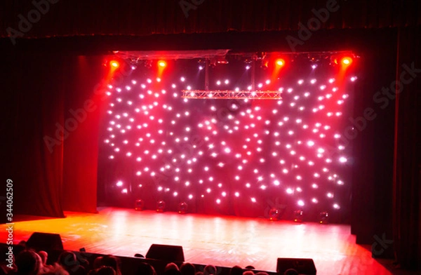 Obraz Blurred show red background. Bright red light beams spotlights on stage at time of entertainment show. Laser and lights show. Empty stage, sparkling stage lights and silhouette shot from back.