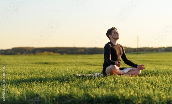 Fototapeta young man doing yoga exercises in the field