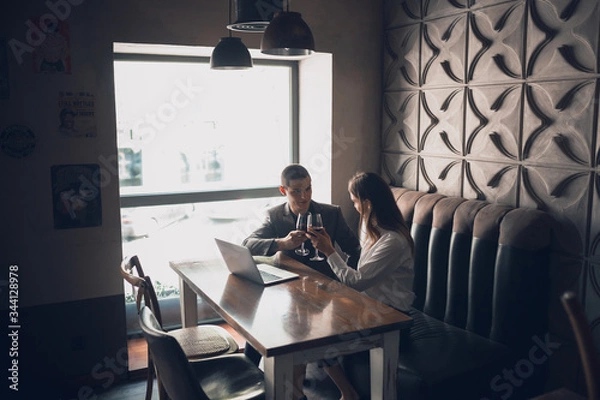 Fototapeta Cheerful man and woman talking, enjoying at the wine shop, cafe. Couple or friends, business partners drinking toghether, sitting at the table in casual attire. Communication, relations concept.