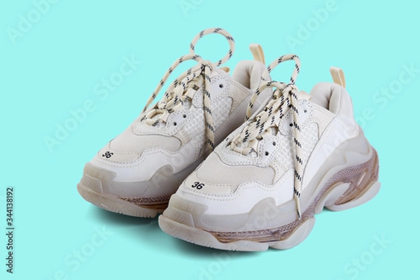 Fototapeta Pair of new trendy beige sneakers isolated on a light blue background with shadow. Top view at an angle.