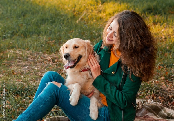 Obraz Smiling woman hugging her pet golden retriever dog near face. Golden retriever dog playing with a curly woman walking outdoors sunny day. love and care for the pet.