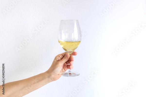 Obraz Woman hand holds gives a glass of champagne white wine on a white background. Place for text.