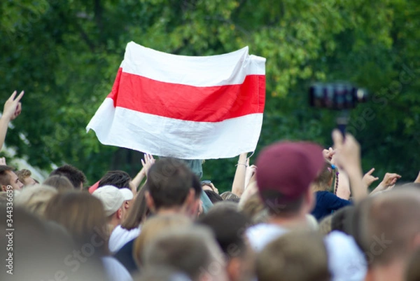 Fototapeta White-red-white flag at a mass event over heads against a background of green foliage of trees. White-red-white flag historical and cultural treasure of Belarus (1918, 1991–1995).