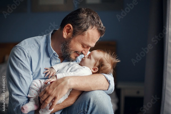 Fototapeta Średnim wieku Caucasion ojciec całuje śpiącą dziewczynę noworodka. Rodzic trzyma na biegunach dziecko córka syna w rękach. Autentyczne chwile rodzicielstwa w stylu życia. Życie rodzinne samotnego ojca.