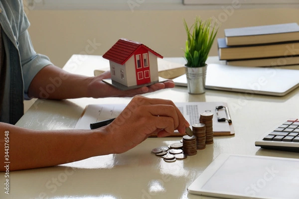 Obraz Saving money concept preset by Male hand putting money coin and signs a contract to purchase a home with a real estate agent. Model house with keys on table.