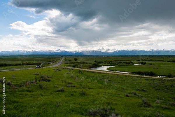 Fototapeta A view of the Teton mountains from several miles north of Victor, Idaho, with green agricultural fields and interesting clouds overhead