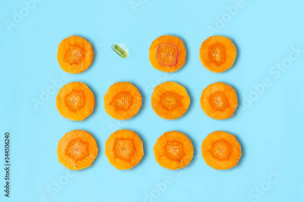 Fototapeta Sliced carrot pattern with capsule on pastel blue background. Fish oil pills. Medicine healthcare or beauty concept. Flat lay style.