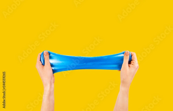 Obraz Blue slime stretchable toy for children in hands. An elastic antistress toy for relaxation. Hands gum. Funny Games. Slime on yellow background. Copy space, place for text.
