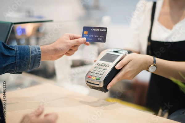 Obraz Hand of man customer using wireless or contactless payment of a credit card. Young Asian cashier or seller are smiling to accept payment by nfc technology at retail shop. Contactless payment concept.
