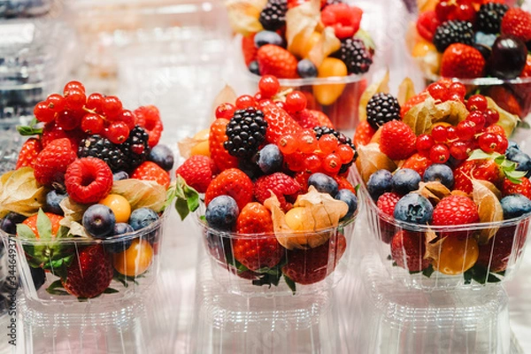 Fototapeta Fruit Salad arranged in plastic cups on a market stall with small fork inside, takeaway snack