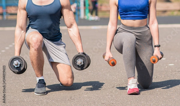 Fototapeta Athletic guy and girl lunges with dumbbells at the playground. Health care.