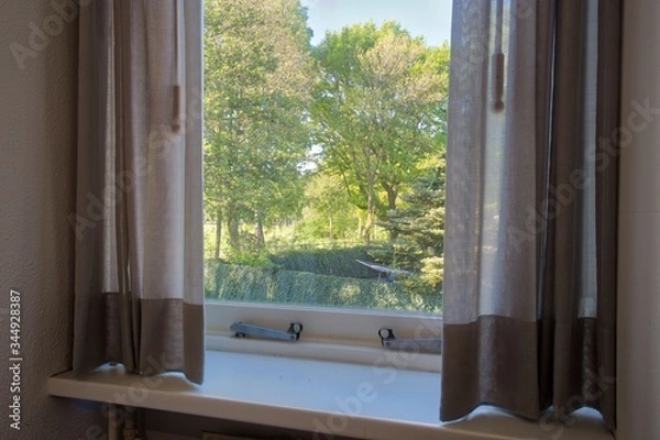 Fototapeta Beautiful green window view with grey curtains in the summer, looking at green forest in nature in a cozy home