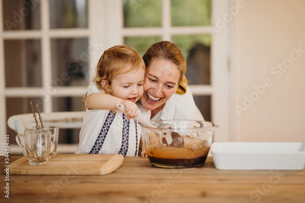 Fototapeta Loving beautiful mother and daughter cooking together a chocolate brownie and having fun