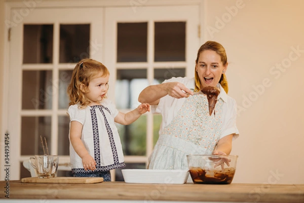 Obraz Loving beautiful mother and daughter cooking together a chocolate brownie and having fun