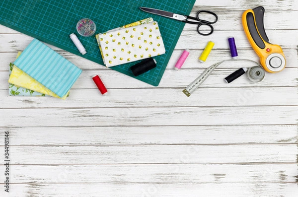 Fototapeta quilting, embroidery and sewing tools on the white wooden background. patchwork knife, scissors, lined cutting mat, self-locking, threads, measuring tape, floss, hoop. copy space. flat lay