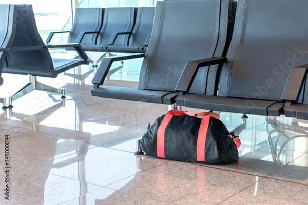 Obraz Suspicious black and red bag left unattended under chair on platform at train station or airportl. Terrorism and public safety concept