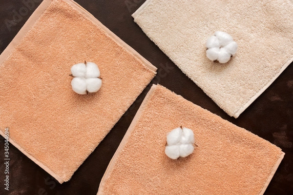 Fototapeta Terry beige towels and cotton flowers on a dark brown rustic background. The concept of natural fabric. Top view, flat lay.