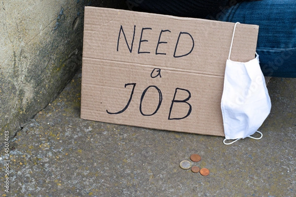 Obraz Unemployment concept and unemployed coronavirus sitting on the ground next to it a cardboard plate with the inscription need a job, the medical hygiene mask and coins